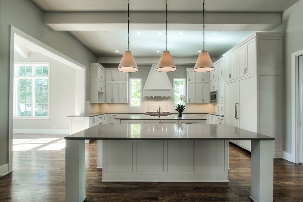 Design ideas for a medium sized traditional u-shaped open plan kitchen in Austin with a submerged sink, shaker cabinets, white cabinets, composite countertops, white splashback, stone tiled splashback, integrated appliances, medium hardwood flooring and multiple islands.