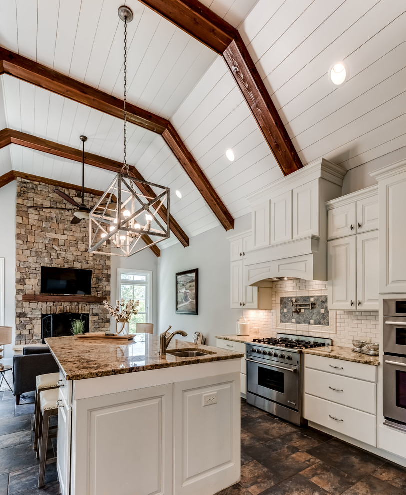 Example of a large country u-shaped travertine floor and brown floor eat-in kitchen design in Grand Rapids with a farmhouse sink, shaker cabinets, white cabinets, granite countertops, white backsplash, subway tile backsplash, stainless steel appliances and an island