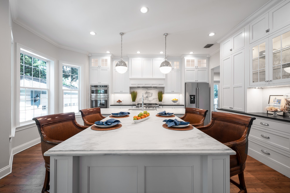 Transitional l-shaped dark wood floor and brown floor kitchen photo in Tampa with an undermount sink, recessed-panel cabinets, white cabinets, white backsplash, stone slab backsplash, an island and white countertops