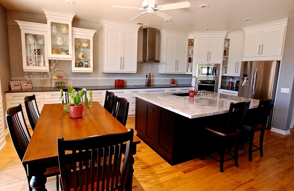 Example of a large transitional l-shaped light wood floor eat-in kitchen design in San Diego with gray backsplash, glass tile backsplash, stainless steel appliances, an island, an undermount sink, shaker cabinets, white cabinets and limestone countertops