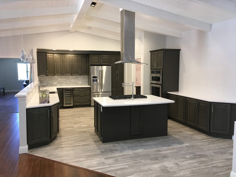 Large minimalist u-shaped porcelain tile and gray floor open concept kitchen photo in Tampa with raised-panel cabinets, gray cabinets, solid surface countertops, gray backsplash, stone tile backsplash, stainless steel appliances and an island