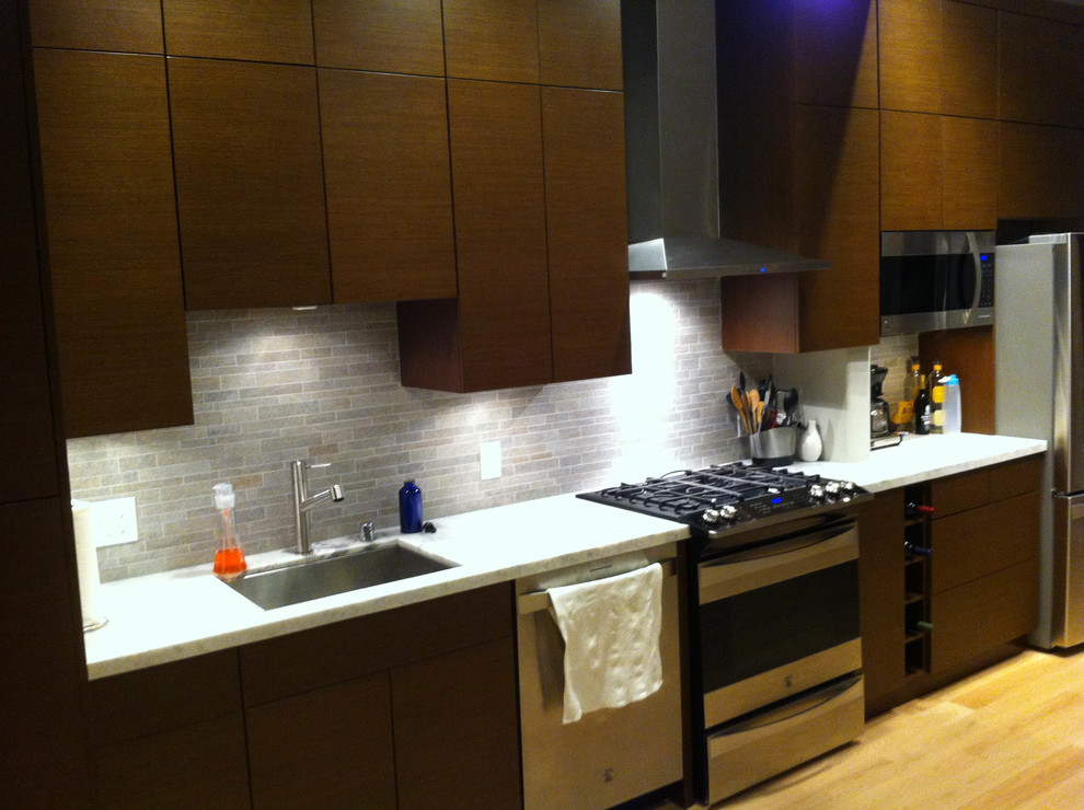 Foto på ett mellanstort funkis linjärt kök med öppen planlösning, med en enkel diskho, släta luckor, bruna skåp, granitbänkskiva, grått stänkskydd, stänkskydd i porslinskakel, rostfria vitvaror, ljust trägolv och en köksö