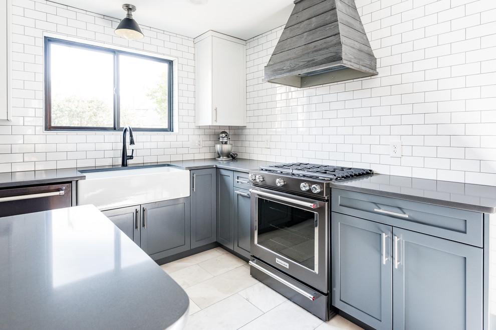 Photo of a large country l-shaped enclosed kitchen in Wilmington with a belfast sink, shaker cabinets, blue cabinets, engineered stone countertops, white splashback, metro tiled splashback, black appliances, marble flooring, an island, grey floors and black worktops.
