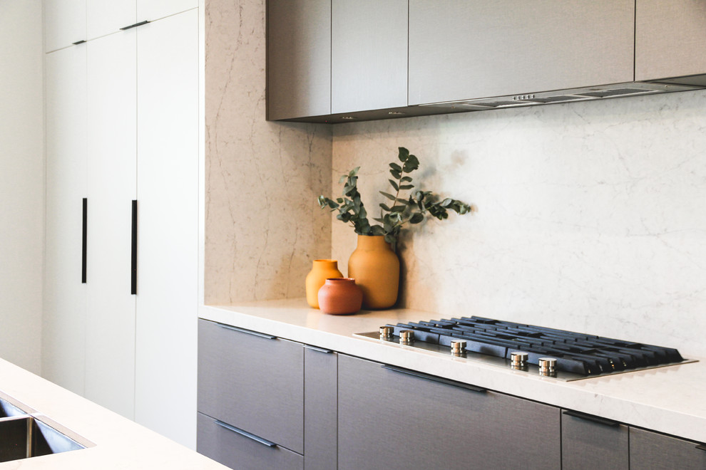 Foto på ett stort funkis vit kök, med en undermonterad diskho, släta luckor, grå skåp, bänkskiva i kvarts, vitt stänkskydd, stänkskydd i sten, integrerade vitvaror, mellanmörkt trägolv, en köksö och svart golv
