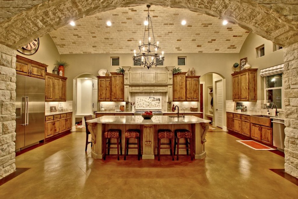 Inspiration for an expansive country galley kitchen/diner in Austin with a belfast sink, raised-panel cabinets, yellow cabinets, granite worktops, beige splashback, stone tiled splashback, stainless steel appliances, concrete flooring and an island.