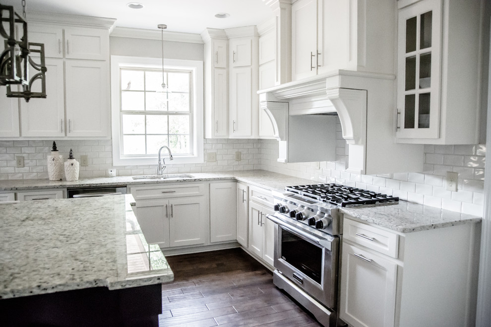 Bild på ett avskilt, mellanstort vintage vit vitt l-kök, med en undermonterad diskho, skåp i shakerstil, vita skåp, bänkskiva i kvartsit, vitt stänkskydd, stänkskydd i tunnelbanekakel, rostfria vitvaror, mörkt trägolv, en köksö och brunt golv