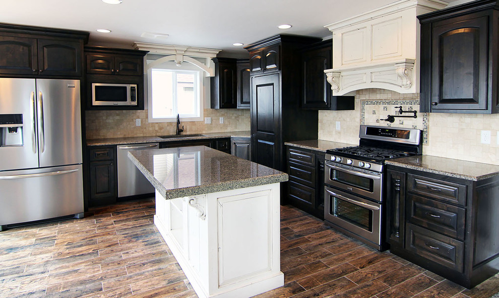 Exempel på ett mellanstort klassiskt flerfärgad flerfärgat kök, med en undermonterad diskho, luckor med upphöjd panel, svarta skåp, granitbänkskiva, beige stänkskydd, stänkskydd i travertin, rostfria vitvaror, mörkt trägolv, en köksö och brunt golv