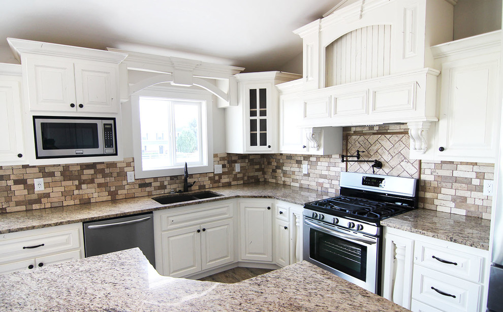 Exempel på ett avskilt, mellanstort klassiskt brun brunt l-kök, med en dubbel diskho, luckor med upphöjd panel, vita skåp, granitbänkskiva, flerfärgad stänkskydd, stänkskydd i stenkakel, rostfria vitvaror och en köksö