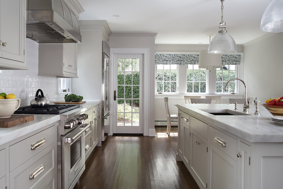 Enclosed kitchen - large transitional l-shaped medium tone wood floor and brown floor enclosed kitchen idea in Newark with an undermount sink, beaded inset cabinets, white cabinets, marble countertops, white backsplash, ceramic backsplash, stainless steel appliances and an island