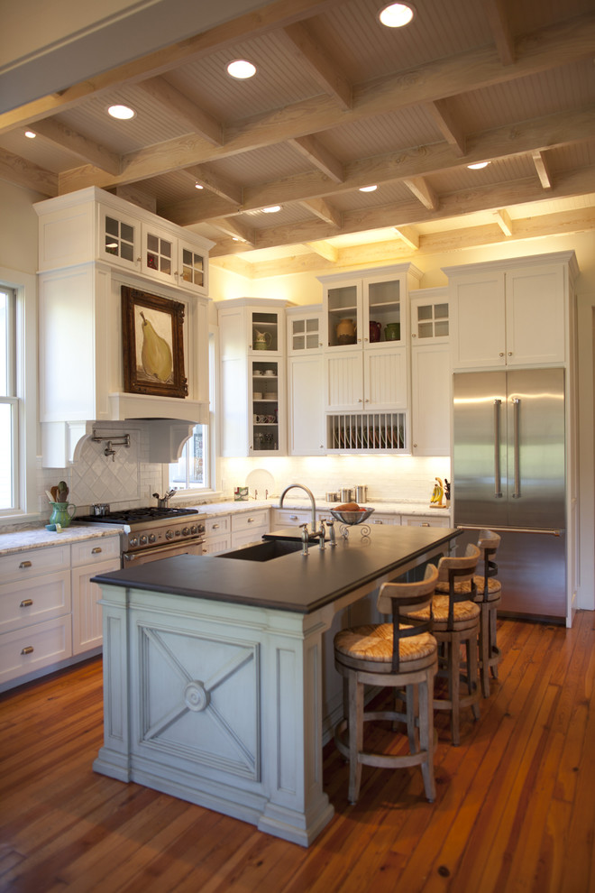 Cette image montre une cuisine traditionnelle en L avec un électroménager en acier inoxydable, un placard à porte shaker, des portes de placard blanches et une crédence blanche.