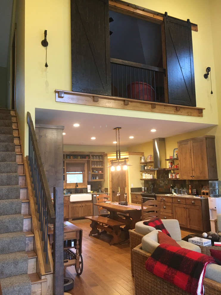 This is an example of a large rustic u-shaped kitchen/diner in Milwaukee with a belfast sink, recessed-panel cabinets, medium wood cabinets, engineered stone countertops, multi-coloured splashback, slate splashback, stainless steel appliances, medium hardwood flooring and beige worktops.