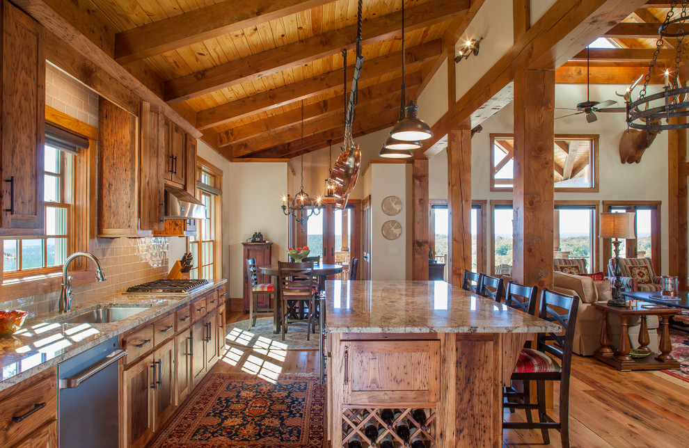 Réalisation d'une grande cuisine ouverte chalet en bois brun avec un placard à porte shaker, un plan de travail en granite, une crédence beige, une crédence en carrelage métro, un électroménager en acier inoxydable, un sol en bois brun, îlot et un évier encastré.