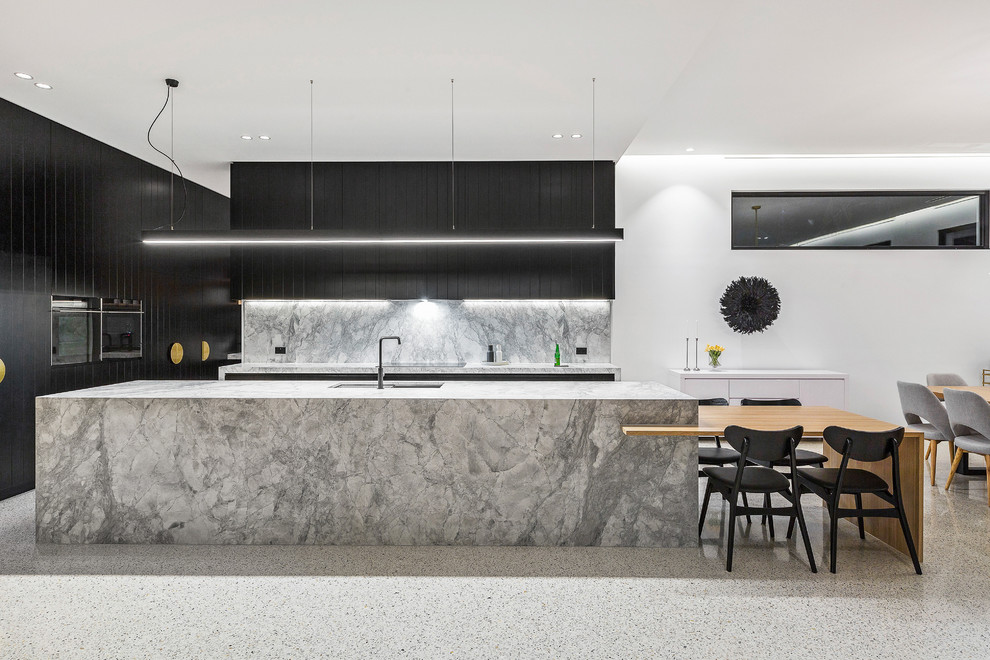 Bild på ett stort funkis grå grått kök, med en undermonterad diskho, släta luckor, svarta skåp, grått stänkskydd, svarta vitvaror, en köksö, marmorbänkskiva, stänkskydd i marmor, betonggolv och vitt golv