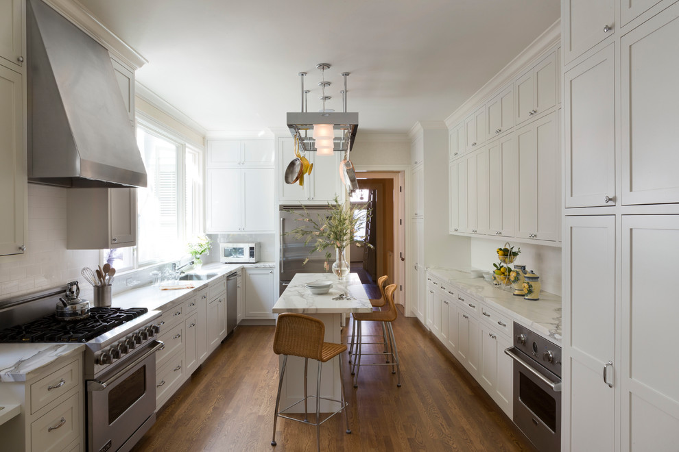 This is an example of a traditional enclosed kitchen in San Francisco with a submerged sink, shaker cabinets, white cabinets, marble worktops, white splashback, metro tiled splashback, stainless steel appliances, medium hardwood flooring, an island and white worktops.