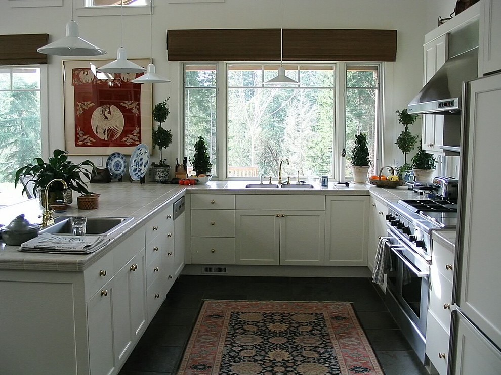 Inspiration for a small world-inspired galley kitchen/diner in Seattle with a double-bowl sink, shaker cabinets, white cabinets, tile countertops, stainless steel appliances, ceramic flooring, a breakfast bar, metallic splashback, metal splashback and grey floors.