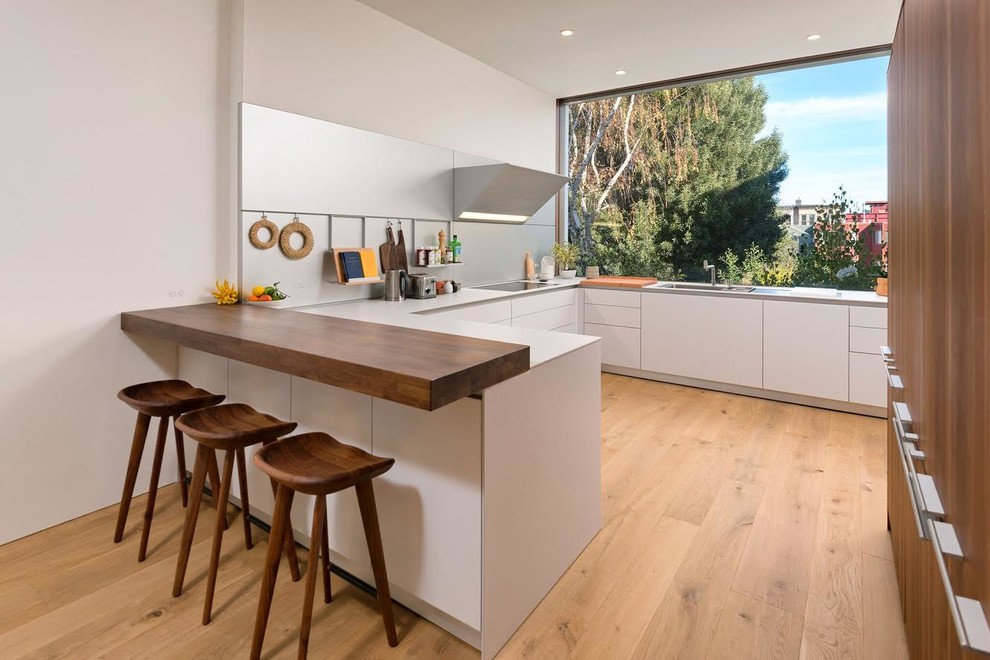 This is an example of a scandi u-shaped kitchen in San Francisco with flat-panel cabinets, white cabinets, metallic splashback, light hardwood flooring, a breakfast bar, beige floors and white worktops.