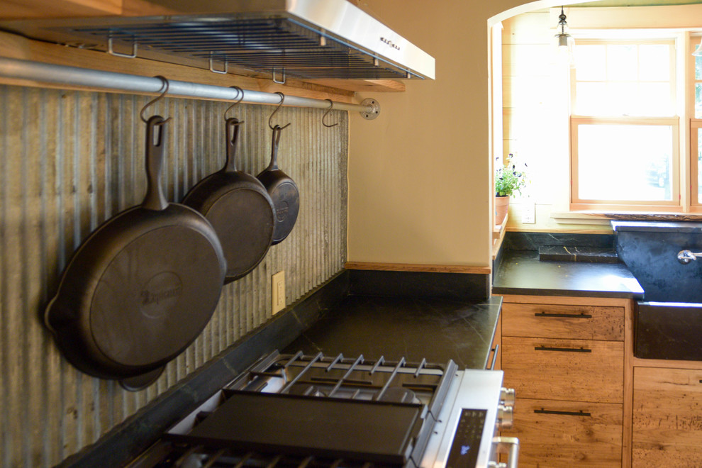 Bild på ett mellanstort amerikanskt svart svart l-kök, med en rustik diskho, släta luckor, skåp i mörkt trä, bänkskiva i täljsten, stänkskydd med metallisk yta, rostfria vitvaror, mellanmörkt trägolv, en köksö och brunt golv