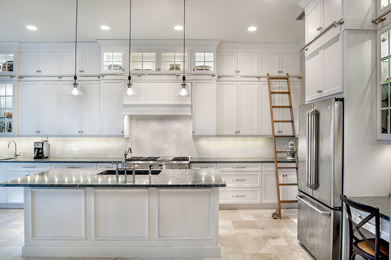 This is an example of a classic kitchen in Miami with a submerged sink, shaker cabinets, white cabinets, soapstone worktops, white splashback, ceramic splashback, stainless steel appliances and travertine flooring.
