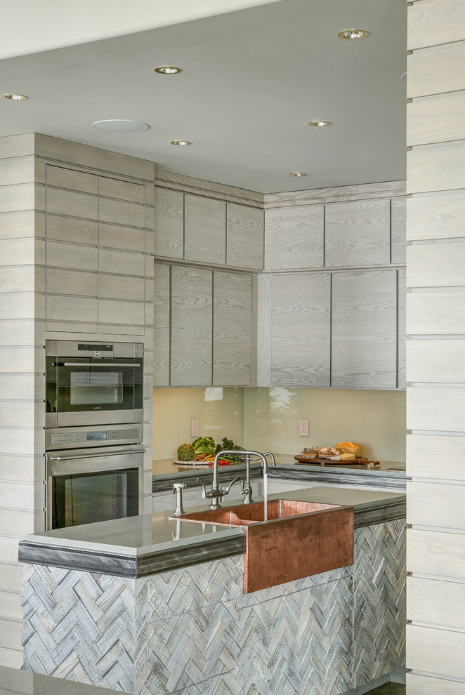 Small trendy u-shaped kitchen photo in Seattle with a farmhouse sink, flat-panel cabinets, light wood cabinets, granite countertops, glass sheet backsplash, stainless steel appliances and an island