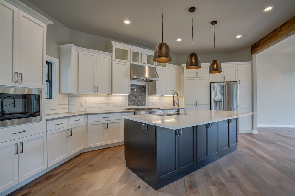 Example of a large transitional galley medium tone wood floor eat-in kitchen design in Other with an undermount sink, recessed-panel cabinets, white cabinets, quartz countertops, white backsplash, ceramic backsplash, stainless steel appliances, an island and gray countertops