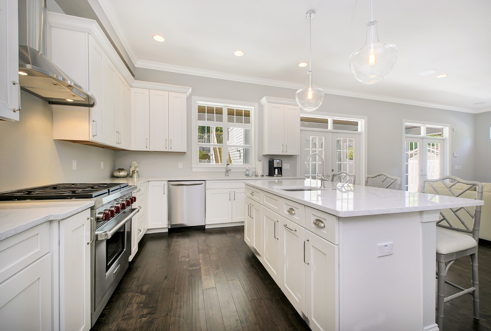 Medium sized coastal u-shaped open plan kitchen in Tampa with a single-bowl sink, shaker cabinets, white cabinets, engineered stone countertops, stainless steel appliances, dark hardwood flooring and an island.