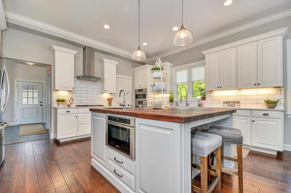 Large transitional u-shaped medium tone wood floor and brown floor eat-in kitchen photo in Tampa with a farmhouse sink, shaker cabinets, white cabinets, quartzite countertops, white backsplash, ceramic backsplash, stainless steel appliances and an island