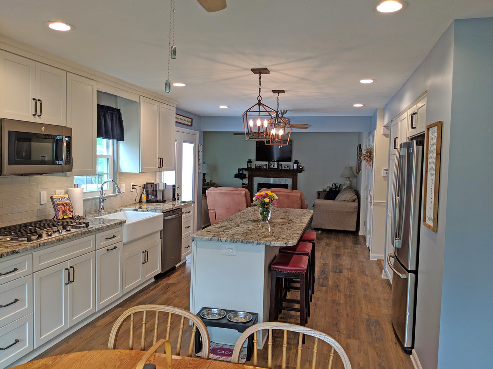 Inspiration for a mid-sized transitional galley vinyl floor and brown floor eat-in kitchen remodel in Baltimore with a farmhouse sink, shaker cabinets, white cabinets, granite countertops, gray backsplash, subway tile backsplash, stainless steel appliances, an island and multicolored countertops
