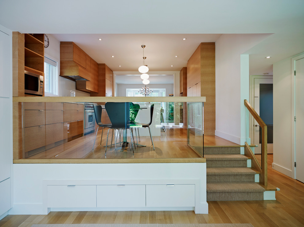 Example of a minimalist galley light wood floor eat-in kitchen design in Toronto with flat-panel cabinets, medium tone wood cabinets, white backsplash, a double-bowl sink, stainless steel appliances, an island and glass sheet backsplash