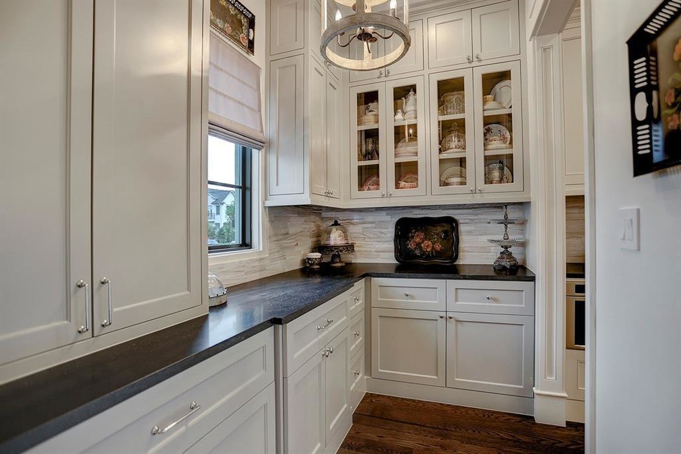 Example of a small classic l-shaped dark wood floor and brown floor kitchen pantry design in Houston with recessed-panel cabinets, white cabinets, quartzite countertops, stainless steel appliances, beige backsplash, porcelain backsplash, no island and black countertops