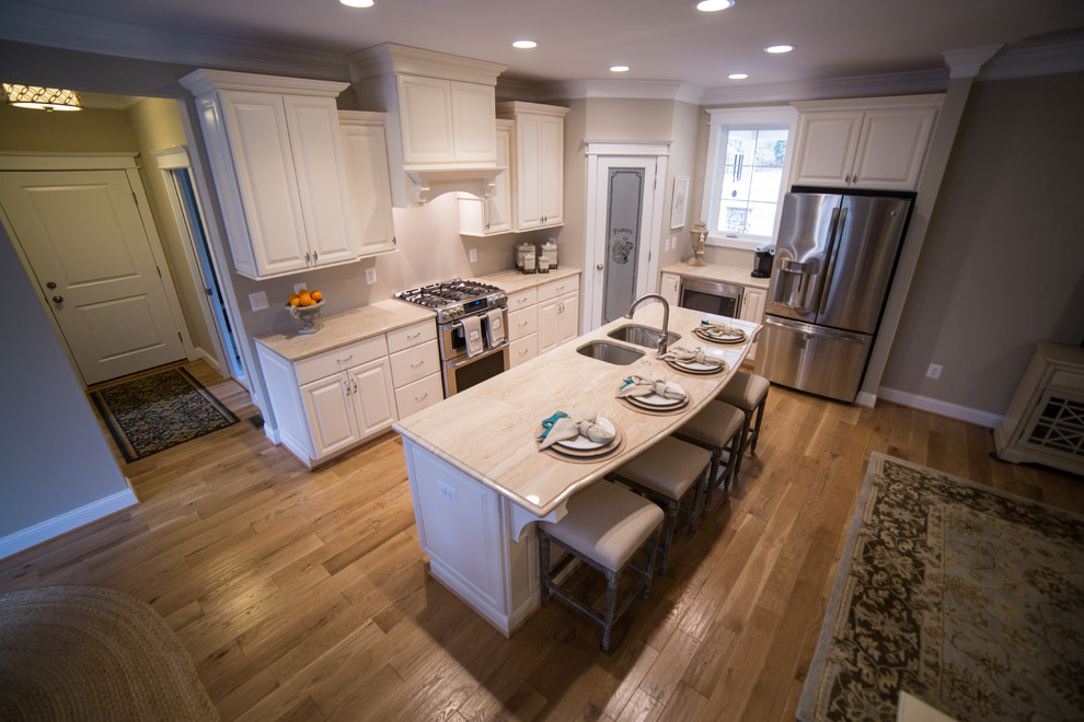Bild på ett stort vintage l-kök, med en undermonterad diskho, luckor med upphöjd panel, vita skåp, granitbänkskiva, rostfria vitvaror, mellanmörkt trägolv, en köksö och brunt golv