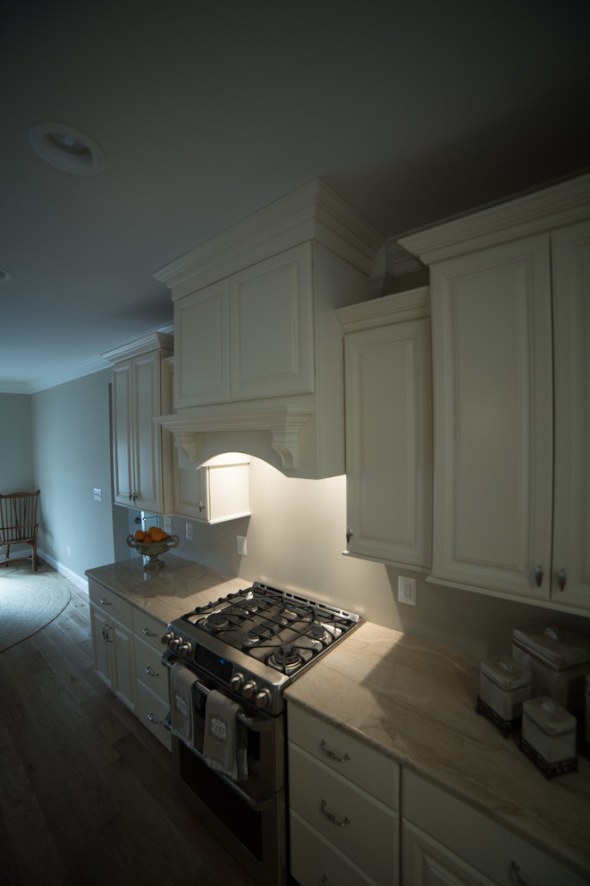 This is an example of a large traditional l-shaped kitchen in DC Metro with a submerged sink, raised-panel cabinets, white cabinets, granite worktops, stainless steel appliances, medium hardwood flooring, an island and brown floors.