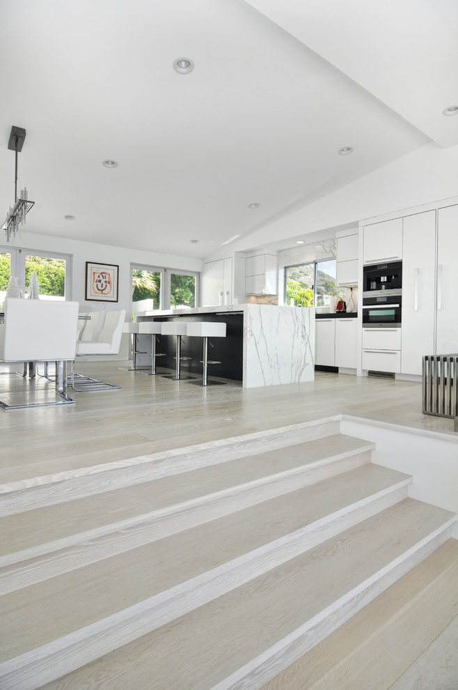 Foto de cocina comedor contemporánea grande con armarios con paneles lisos, encimera de mármol, salpicadero de losas de piedra, suelo de madera en tonos medios, una isla y puertas de armario blancas