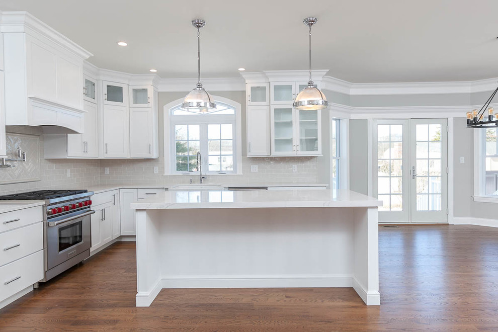 Inspiration for a large u-shaped medium tone wood floor and brown floor kitchen pantry remodel in New York with a farmhouse sink, shaker cabinets, white cabinets, quartzite countertops, gray backsplash, subway tile backsplash, stainless steel appliances, an island and white countertops