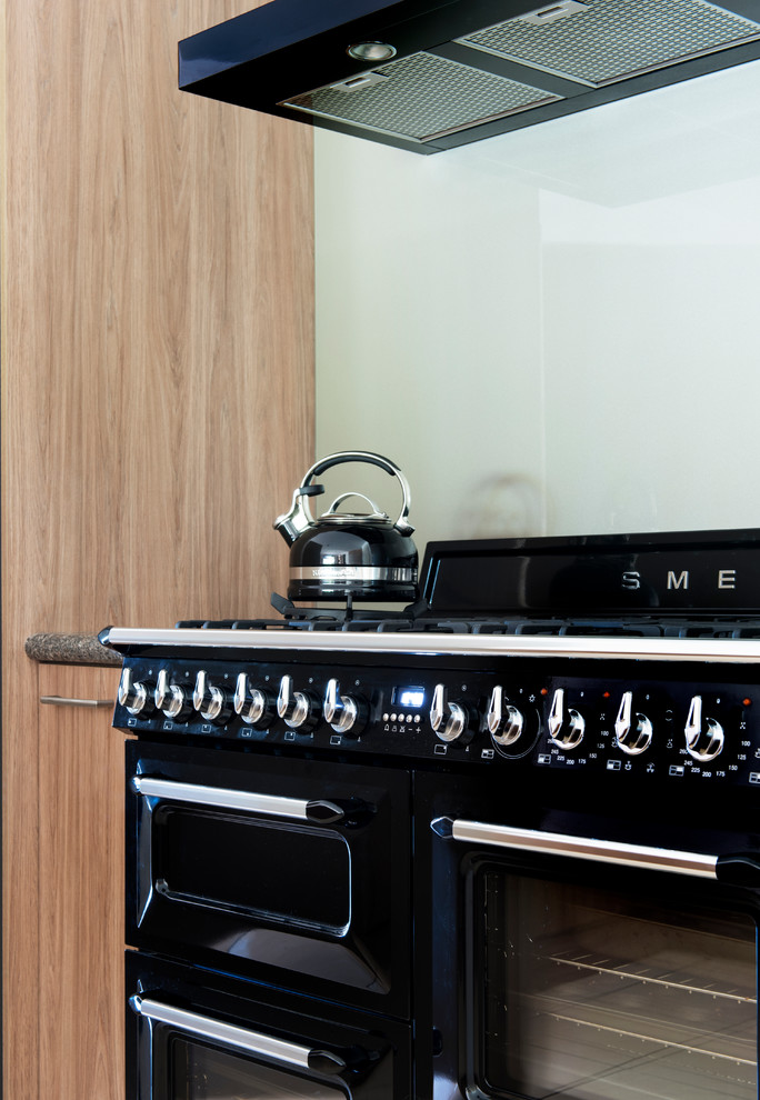Diseño de cocina moderna de tamaño medio con puertas de armario de madera clara, encimera de cuarzo compacto, salpicadero blanco, salpicadero de vidrio templado y electrodomésticos negros
