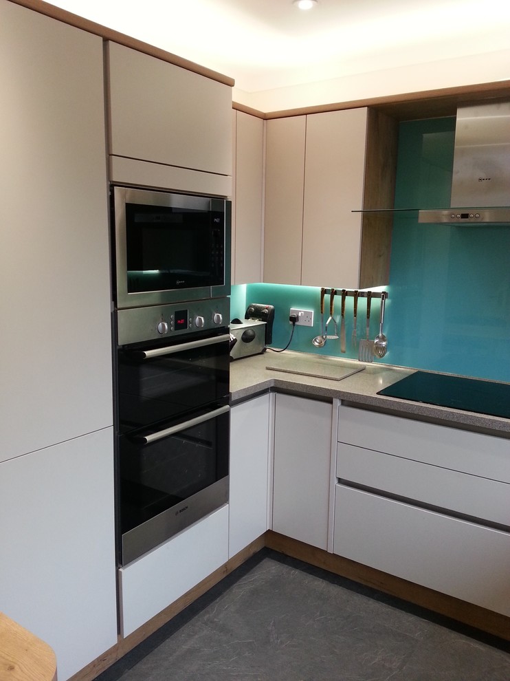 Photo of a modern l-shaped kitchen/diner in Glasgow with flat-panel cabinets, blue splashback, glass sheet splashback, integrated appliances and no island.