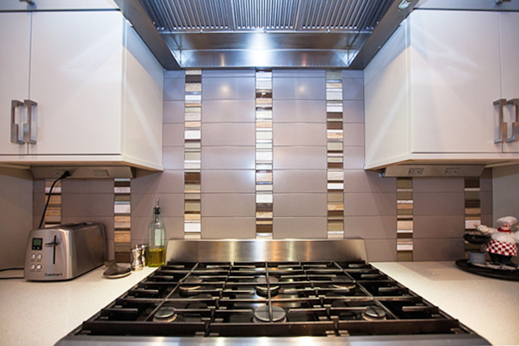 Inredning av ett modernt stort linjärt kök och matrum, med en undermonterad diskho, luckor med infälld panel, grå skåp, bänkskiva i kvarts, grått stänkskydd, glaspanel som stänkskydd, rostfria vitvaror, mellanmörkt trägolv och flera köksöar