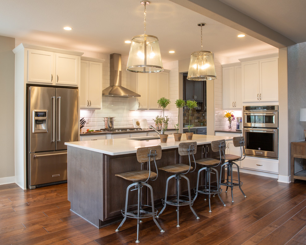 Inspiration for a large transitional u-shaped medium tone wood floor and brown floor open concept kitchen remodel in Denver with an undermount sink, shaker cabinets, white cabinets, quartzite countertops, white backsplash, porcelain backsplash, stainless steel appliances, an island and white countertops