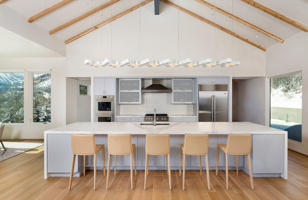 Foto på ett stort funkis kök, med luckor med glaspanel, skåp i rostfritt stål, marmorbänkskiva, vitt stänkskydd, rostfria vitvaror, ljust trägolv, en köksö och brunt golv