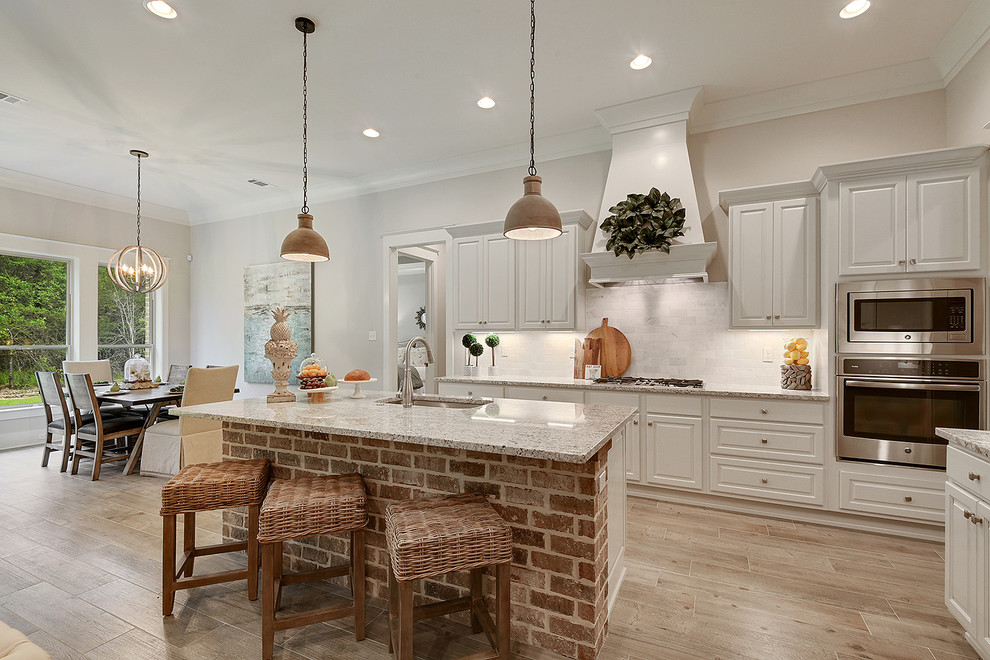 Inspiration for a medium sized rustic l-shaped open plan kitchen in New Orleans with a submerged sink, raised-panel cabinets, white cabinets, granite worktops, grey splashback, stone tiled splashback, stainless steel appliances, light hardwood flooring, an island and beige floors.