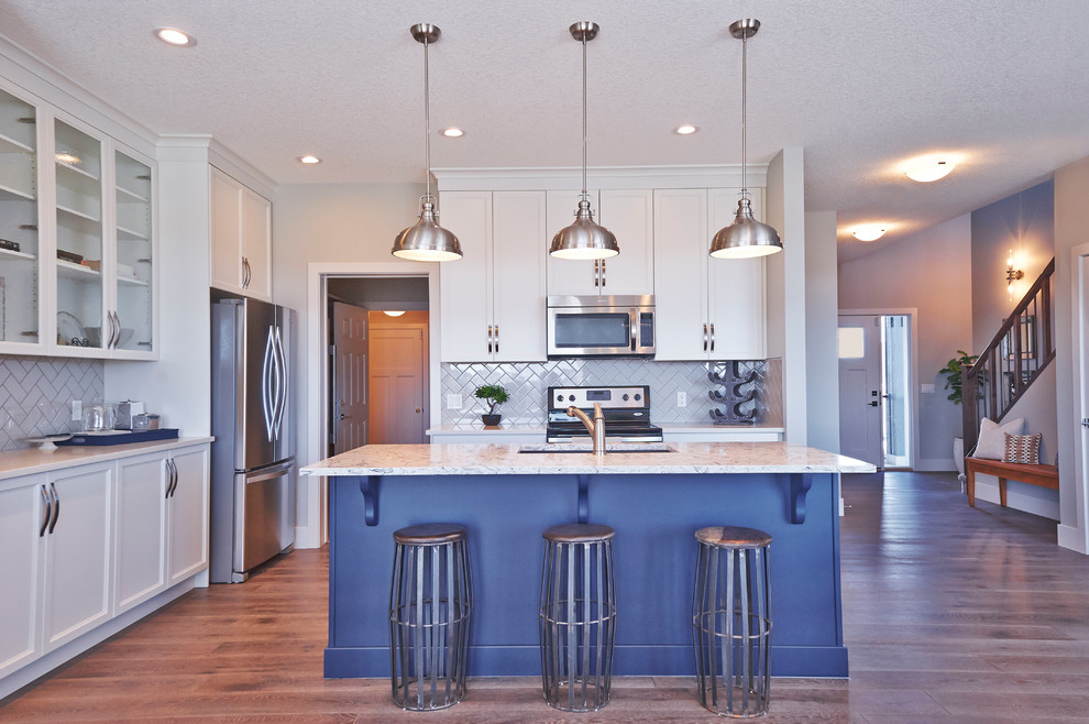 This is an example of a traditional l-shaped kitchen/diner in Calgary with a double-bowl sink, shaker cabinets, blue cabinets, quartz worktops, grey splashback, ceramic splashback, stainless steel appliances, medium hardwood flooring and an island.