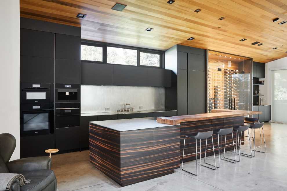 Foto di una grande cucina minimalista con lavello integrato, ante lisce, ante nere, top in acciaio inossidabile, elettrodomestici neri e pavimento in cemento