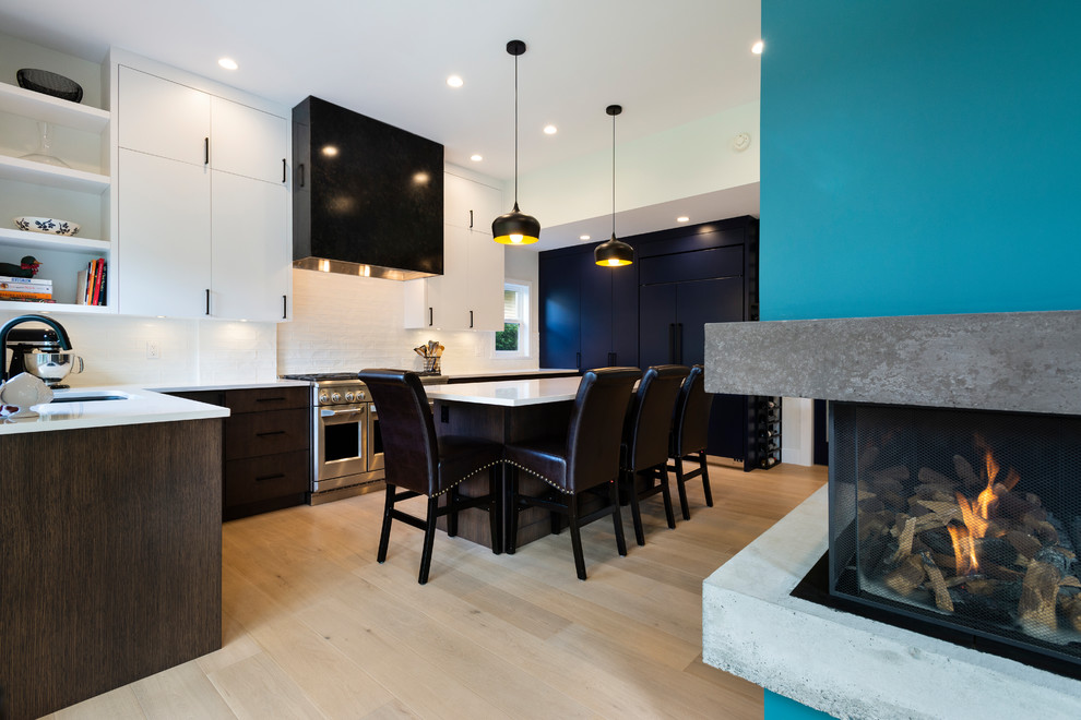 This is an example of a medium sized contemporary u-shaped open plan kitchen in Vancouver with a submerged sink, flat-panel cabinets, engineered stone countertops, white splashback, porcelain splashback, integrated appliances, light hardwood flooring, an island, beige floors and white worktops.