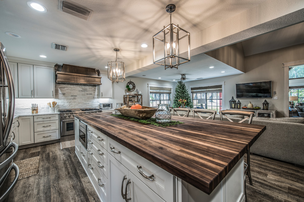 Eat-in kitchen - large rustic u-shaped vinyl floor and brown floor eat-in kitchen idea in Tampa with a farmhouse sink, recessed-panel cabinets, white cabinets, wood countertops, white backsplash, stone tile backsplash, stainless steel appliances and an island