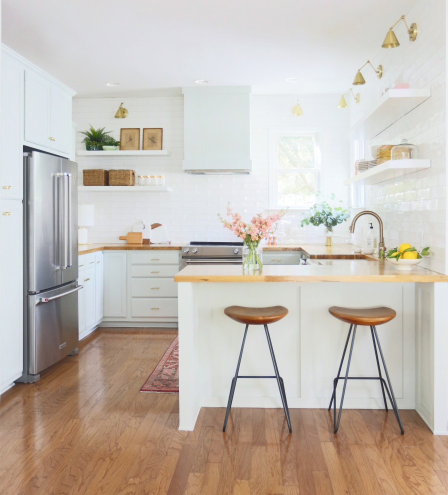 Design ideas for a romantic u-shaped kitchen in Atlanta with a belfast sink, white cabinets, wood worktops, white splashback, stainless steel appliances, medium hardwood flooring and a breakfast bar.