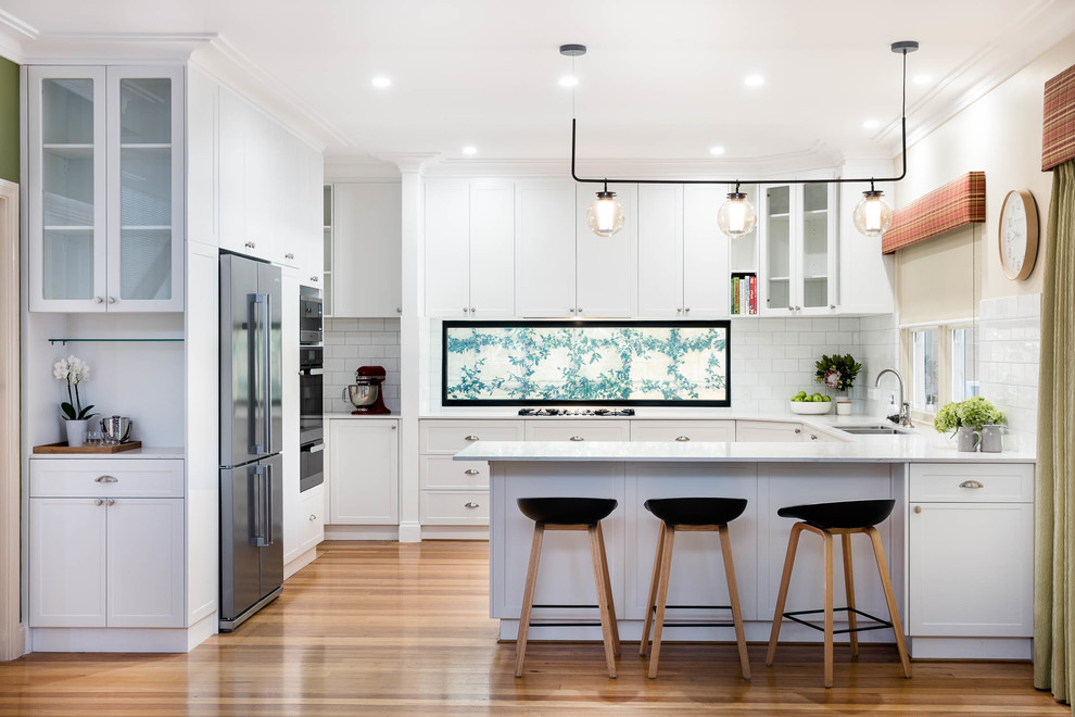 This is an example of a traditional u-shaped kitchen in Perth with marble worktops, white splashback, metro tiled splashback, light hardwood flooring, flat-panel cabinets, white cabinets, stainless steel appliances, no island and brown floors.