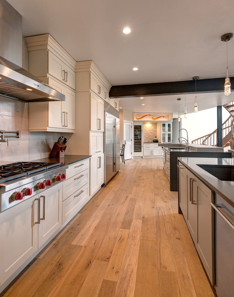 Traditional galley open plan kitchen in Denver with a double-bowl sink, shaker cabinets, white cabinets, engineered stone countertops, beige splashback, stone tiled splashback, stainless steel appliances, medium hardwood flooring, multiple islands and brown floors.