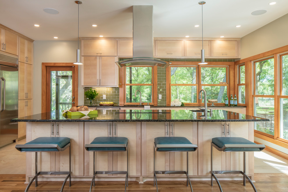 Photo of a medium sized contemporary kitchen in Austin with flat-panel cabinets, light wood cabinets, granite worktops, green splashback, glass tiled splashback, stainless steel appliances and an island.