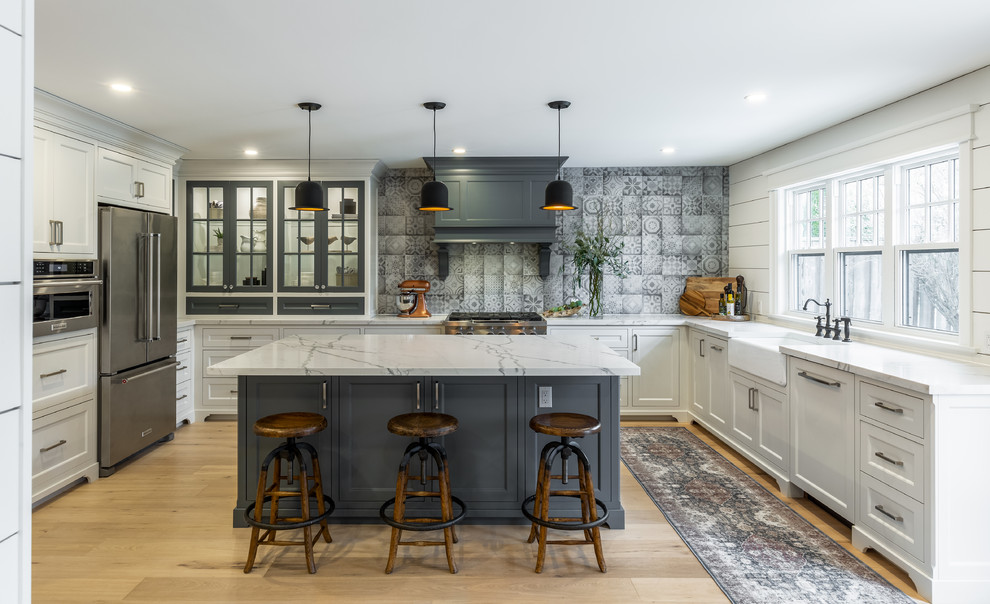 Design ideas for a medium sized country u-shaped kitchen/diner in Toronto with a belfast sink, white cabinets, engineered stone countertops, grey splashback, porcelain splashback, stainless steel appliances, light hardwood flooring, an island and white worktops.