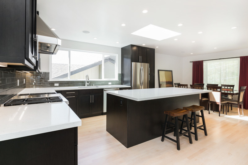 Modern inredning av ett stort kök, med en integrerad diskho, bänkskiva i kvarts, rostfria vitvaror, skåp i shakerstil, svarta skåp, ljust trägolv och en köksö