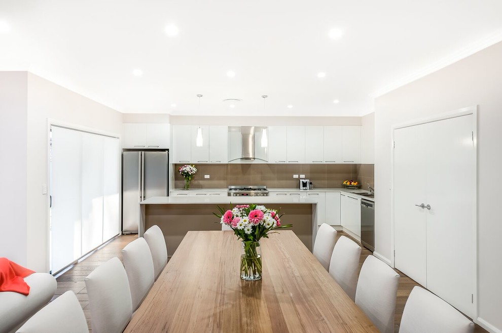 Design ideas for a large modern galley kitchen/diner in Sydney with a double-bowl sink, white cabinets, engineered stone countertops, beige splashback, ceramic splashback, stainless steel appliances, medium hardwood flooring and an island.